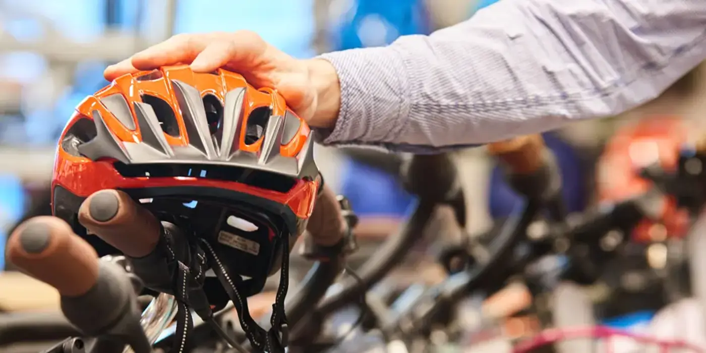 Hand som håller i en orange cykelhjälm, med cyklar i bakgrunden.