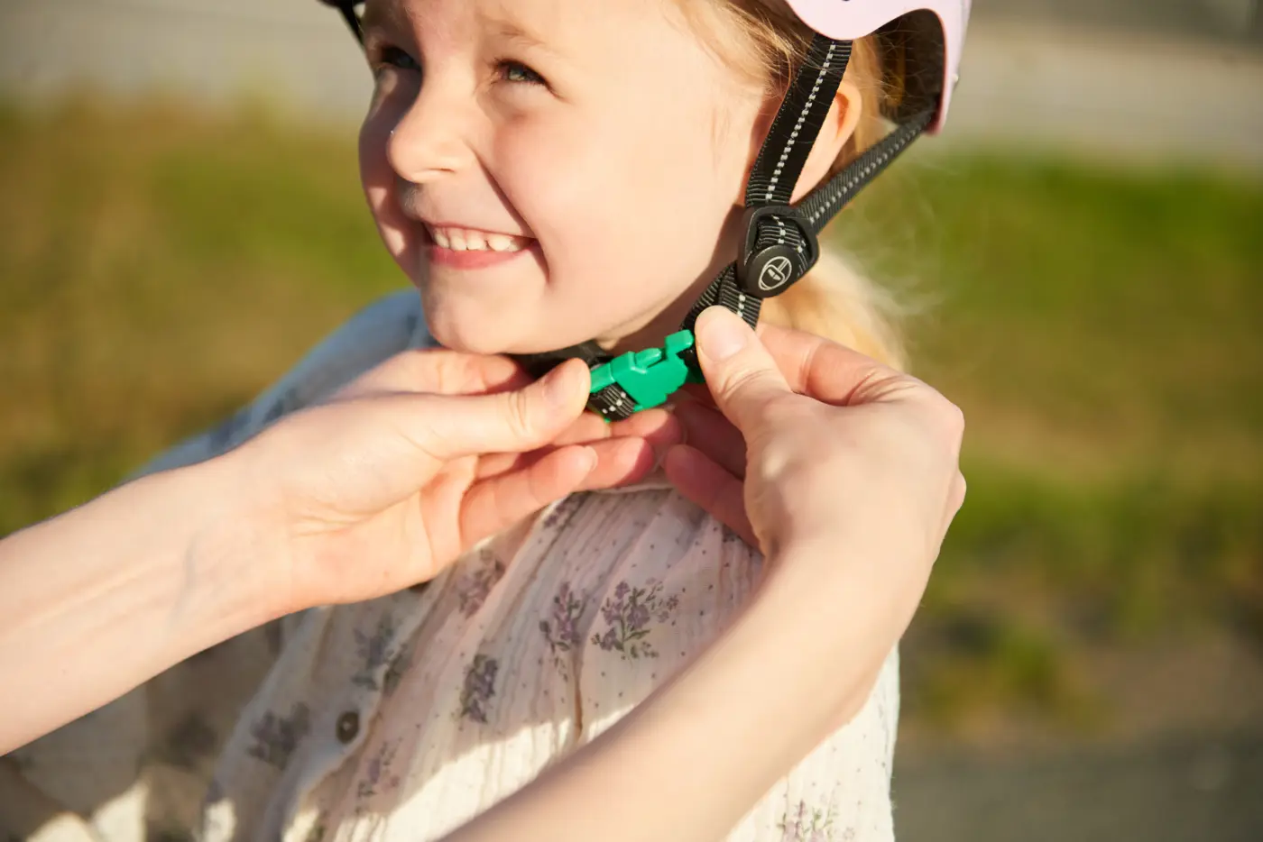 Ett barn får hjälp att knäppa sin cykelhjälm med grönt spänne.